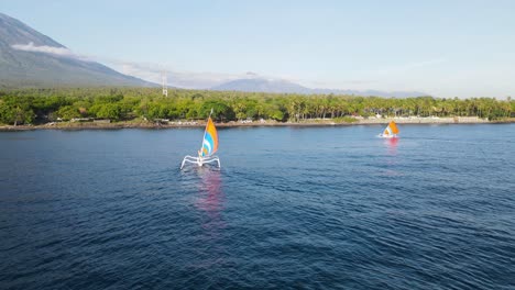Traditionelle-Balinesische-Fischerboote-Segeln-Zu-Den-Küstenstränden,-Die-Von-Der-Hoch-Aufragenden-Vulkankulisse-In-Den-Schatten-Gestellt-Werden