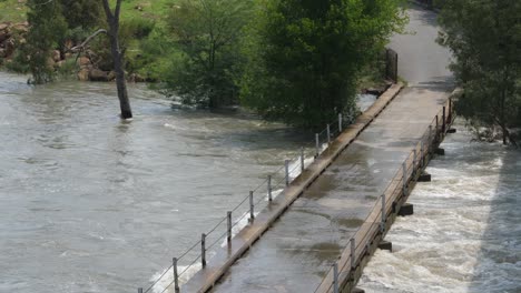 Flood-water-of-muddy-fast-river-at-deck-of-low-single-lane-bridge