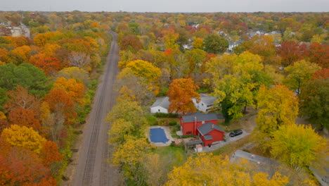 Aerial-over-train-tracks-through-neighborhood-in-Kirkwood,-Missouri-in-Autumn-at-peak-Fall-color-on-a-beautiful-day