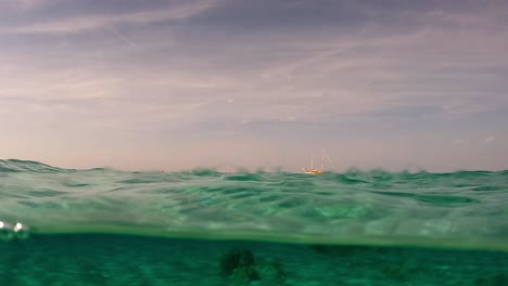 Half-under-water-view-of-sailing-ship-moored-at-horizon-and-clear-transparent-seawater-with-rocks-on-sea-floor