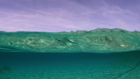 Halb-Unter-Wasser-Blick-Auf-Ein-Segelschiff,-Das-Am-Horizont-Festgemacht-Ist,-Und-Klares,-Transparentes-Meerwasser-Mit-Küste-Im-Hintergrund