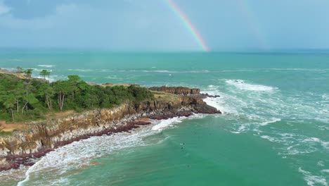 Drone-shot-of-big-waves-cutting-at-the-cliffs-with-a-rainbow-in-the-background