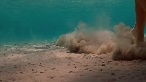 Under-water-scene-of-little-girl-jumps-on-seabed-raising-clouds-of-sand-in-transparent-water