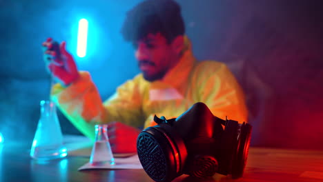 scientist-in-hazmat-suit-working-on-his-desktop-lab-experimenting-with-chemical-substances-dropping-dangerous-liquid-in-sterilises-container,-respiratory-mask-in-foreground-blue-led-light-foreground