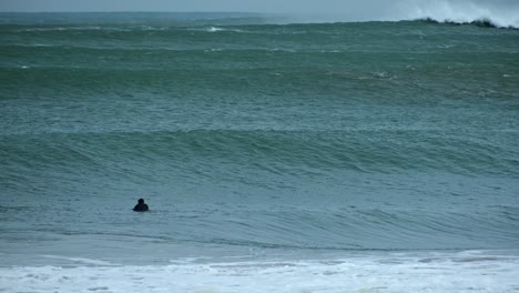 Two-unrecognizable-man's-figure-with-a-surf-in-front-of-big-waves-braking-on-a-beach