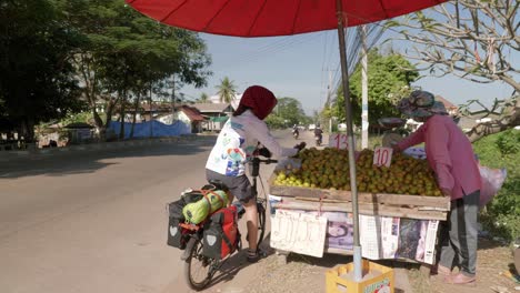 Frau-Auf-Dem-Fahrrad,-Die-Frisches-Obst-Vom-Lokalen-Straßenstand-In-Südostasien-Pflückt