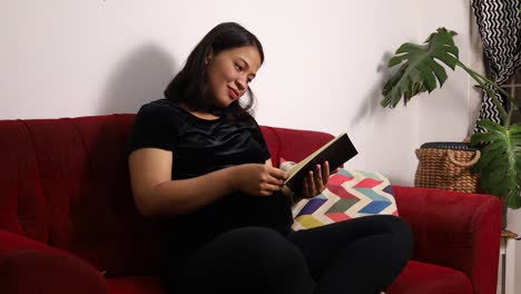 Feliz-Mujer-Asiática-Embarazada-Leyendo-Un-Libro-En-Casa