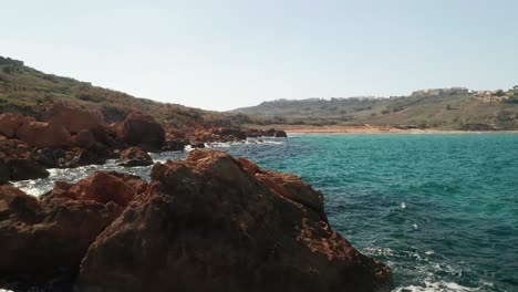 Toma-Aérea-De-Una-Costa-Con-Hermosas-Rocas-De-Color-Rojo-Y-Aguas-Turquesas-Del-Mar-Mediterráneo,-Playa-De-Ramla-En-La-Isla-De-Gozo,-Malta
