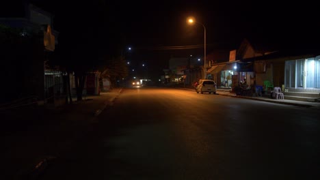 Vehicles-circulating-at-night-in-dark-road-of-Kenethao-asian-town,-Laos
