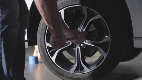 Unrecognizable-mechanic-using-lug-wrench-to-remove-lug-nuts-from-car-wheel,-slow-motion