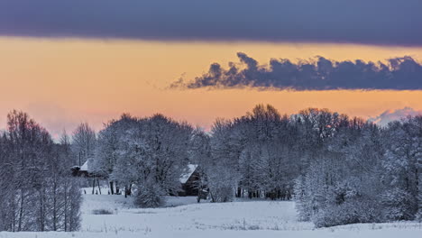 Timelapse-shot-of-sunset-during-evening-time-along-snow-covered-ground-beside-village-houses-with-clouds-passing-by