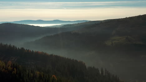 Morning-flight-over-foggy-Hasmas-Mountains,-village-of-Balan-in-valley,-Romania