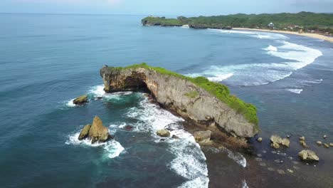 Drone-view-of-shoreline-with-huge-coral-rock-with-clusters-of-small-rocks-that-crushing-by-the-wave-on-the-tropical-beach