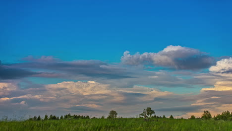 Shot-of-white-cirrus-cloud-movement-in-timelapse-across-bllue-sky-over-green-grasslands-on-a-cloudy-day