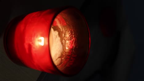 Static-shot-of-a-bright-red-candle-glowing-and-burning-out-as-wax-gets-low-with-the-words-"pumpkin-apple"-visible-through-the-glow-of-the-glass-and-a-lighter-and-candle-cap-visible-in-the-blurred-back