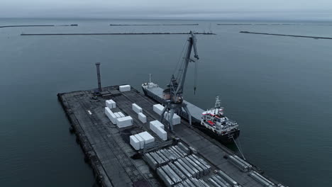 Aerial-drone-rotating-shot-over-shipping-containers-being-been-loaded-onto-a-container-ship-in-a-harbour-during-evening-time