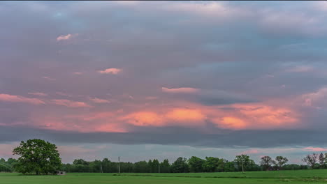 Static-shot-of-rainy-clouds-passing-by-in-timelapse-over-rural-countryside-with-young-green-wheat-sprouts-in-summer-evening