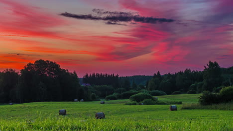 Amazing,-colorful-sunrise-over-farmland-fields-with-freshly-baled-rolls-of-hay---dramatic-time-lapse-cloudscape