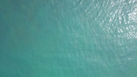 Überkopfdrohnenaufnahme-Einer-Ruhigen-Bläulichen-Meeresoberfläche-Mit-Reflexion-Des-Sonnenlichts