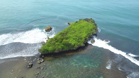 Aerial-view-of-big-coral-rock-on-the-shoreline-with-clear-sea-water-and-waves