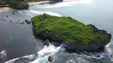 Luftbild-Eines-Riesigen-Korallenfelsens,-Der-Mit-Grasvegetation-Am-Strand-Bewachsen-Ist-Und-Von-Der-Welle-Zerquetscht-Wird