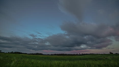 Low-angle-shot-of-dark-cloud-movement-in-timelapse-over-green-grasslands-with-the-silhouette-of-forest-trees-in-the-background
