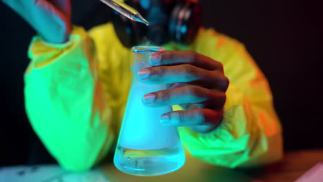 yellow-hazmat-suit-Scientist-hold-laboratory-glass-container-dropping-transparent-liquid-while-wearing-respiratory-gas-mask,-dangerous-experiment-close-up-of-chemist-working-hands