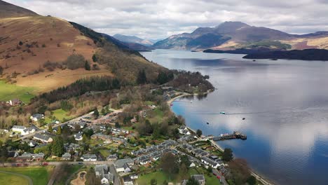 Aerial-Pullback-Angle-Around-The-Village-Of-Luss-On-Loch-Lomond-Over-The-Water-To-Reveal-Village-In-Early-Spring