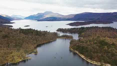 Aerial-drone-angle-of-boats-travelling-through-the-narrows-on-Loch-Lomond,-Scotland,-with-Luss-and-Ben-Lomond-in-the-background-in-early-spring