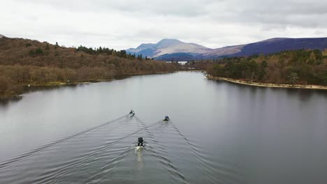 Cinematic-slowmo-aerial-view-of-a-flyby-of-3-boats-approaching-the-narrows-on-Loch-Lomond-in-Scotland,-lifting-up-to-reveal-Ben-Lomond