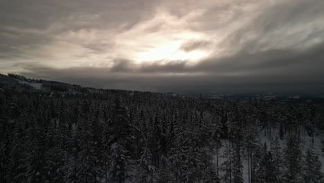 Drone-flying-over-a-winter-landscape-with-the-sun-peering-through-the-clouds-in-the-distance