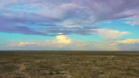 Drone-over-desert-with-clouds-and-rainbow,-low-brush