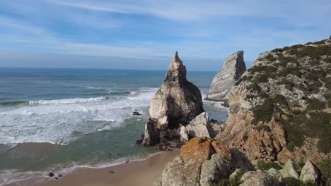 Panning-shot-of-Praia-da-Ursa-beach-and-cliffside-with-rough-seas-and-blue-skies