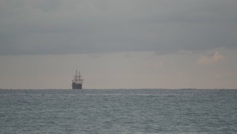 16th-Century-Galleon-Andalucia-replica-ship-sailing-in-the-distance-in-the-Mediterranean-sea-in-a-dark-cloudy-day-at-sunrise