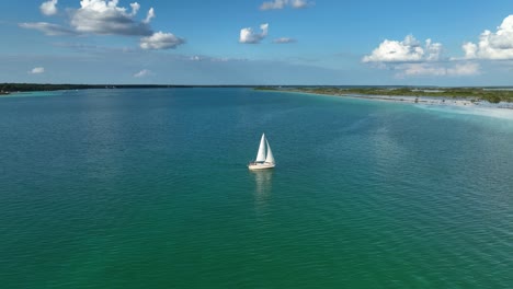 Aerial-view-approaching-a-sailboat-in-turquoise-lake-waters-at-the-laguna-Bacalar,-sunny-Mexico