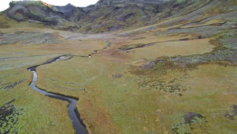 Volando-Sobre-El-Paisaje-Islandés-Cubierto-De-Musgo-Con-Un-Largo-Río-Que-Corre-Hasta-El-Pico-De-La-Montaña-En-El-Oeste-De-Islandia