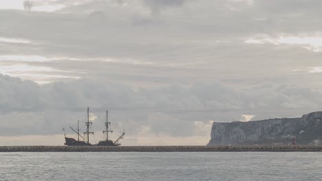16th-Century-Galleon-Andalucia-replica-ship-arriving-at-port-in-a-beautiful-cloudy-day-at-sunrise-behind-a-breakwater-with-mountain-in-the-background