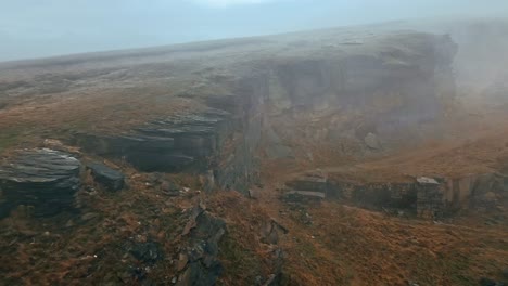 Aerial-view-of-an-amazing-mist-moving-over-the-cliff-tops,-foggy-golden-hills-and-beautiful-rocky-cliffs-and-moorlands