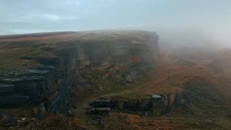 Aerial-drone-view-of-an-clouds-moving-over-the-hills,-Pennines-on-a-foggy-morning,-golden-hills-and-beautiful-rocky-cliffs-and-moorlands