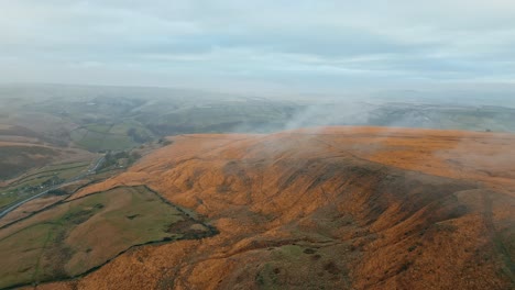 Aerial-view-of-an-clouds-moving-over-the-hills,-Pennines-on-a-foggy-morning,-golden-hills-and-beautiful-rocky-cliffs-and-moorlands