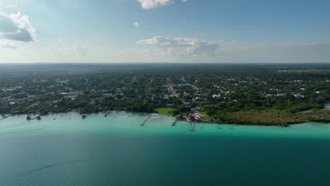 Aerial-view-overlooking-the-Bacalar-town,-in-sunny-Mexico---tracking,-drone-shot