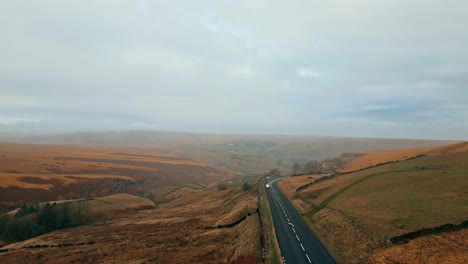 Road-across-the-bleak-exposed-and-windswept-Pennine-moorland-above-Huddersfield-Yorkshire-England-with-a-single-car-traveling-along