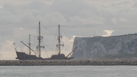 16th-Century-Galleon-Andalucia-replica-ship-arriving-at-port-in-a-cloudy-day-at-sunrise-behind-a-breakwater-with-mountain-in-the-background
