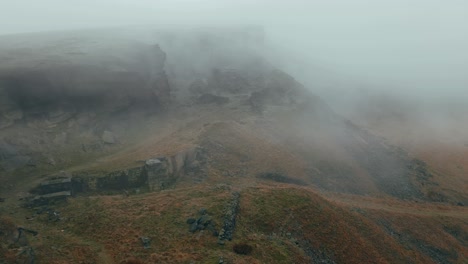 Aerial-drone-view-of-clouds-moving-slowly-over-the-Pennine-hills,-on-a-foggy-morning,-golden-hills-and-beautiful-rocky-cliffs-and-moorlands