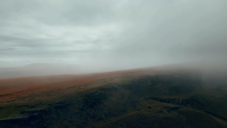 Aerial-drone-view-of-morning-mists-moving-slowly-over-the-damp-rugged-Pennine-hills,-on-a-foggy-morning,-golden-hills-and-beautiful-rocky-cliffs-and-moorlands
