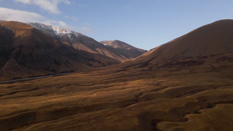 Luftbild---Goldene,-Wellige-Ebenen-Vor-Schneebedeckten-Hügeln-In-Mackenzie,-Neuseeland