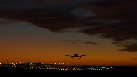 Plane-landing-on-illuminated-runway-at-Barcelona-airport-at-dramatic-sunset