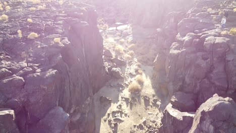 Tilt-down-shot-over-rocky-terrain-with-large-rocks-and-boulders-along-canyon-with-dry-riverbed-with-barren-mountains-in-the-background-on-a-bright-sunny-day