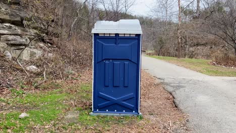 static-video-of-a-blue-porta-potty-in-a-park-with-dead-trees-and-asphalt-roads