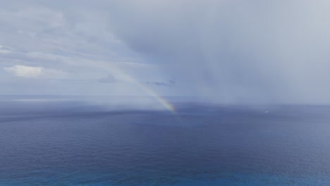 Aerial-view-of-a-distant-rainbow-on-the-sea-in-rainy-Mexico---tracking,-drone-shot